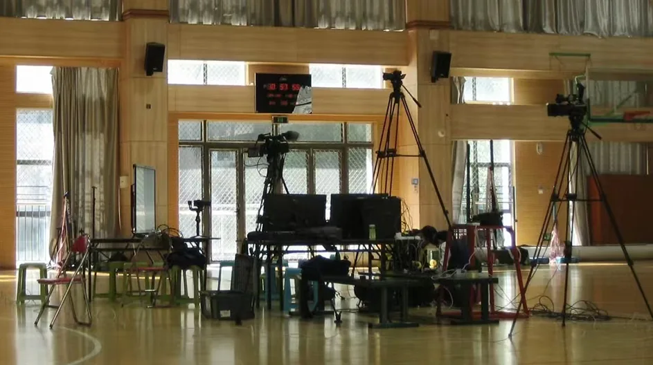 Cameras on tripods and the production desk set up inside the school hall